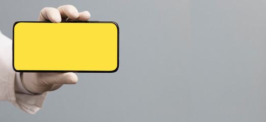 black phone in doctor hand with yellow screen for mockup, gray background