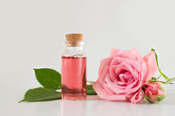 Obraz na płótnie Canvas A glass jar with a pink rose. Cosmetics and perfume. Scented rose water in a glass bottle, roses. Flatly composition with a glass vessel and rose flowers on a pink background, space for text