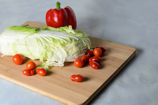 Vegetables on a chopping board. Red bell pepper, tomatoes, petsai cabbage on a board.