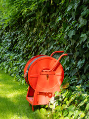 Bright red fire hose in garden. Flexible hose for water supply in case of fire. Preventive measures to prevent natural disasters from flame.