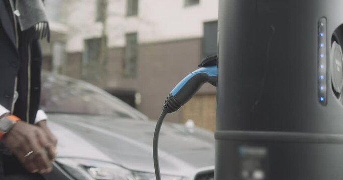 Close up of Business man charging electric car at charging station in city wearing smart watch