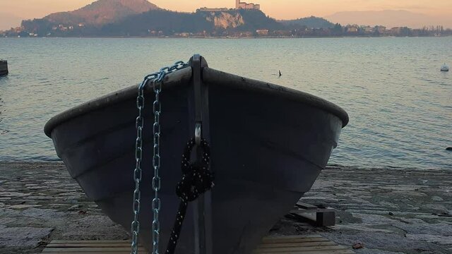 Fishing boat aground and tied with iron chain facing Lake Maggiore and Angera castle, Arona, Italy