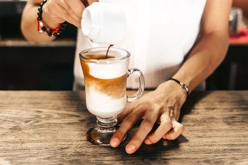 Fototapeta na wymiar hands of a barista or waiter making a coffee or cappucino by adding coffee to a glass tumbler with milk.