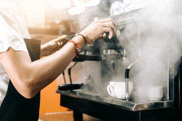 unrecognizable person manipulating a machine to make coffee and that makes steam.