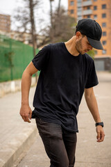 Young caucasian male from Italy in a black shirt and cap walking on the street