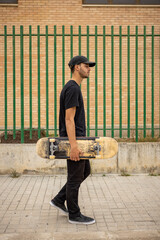 Young male in a black shirt and cap holding a skate in his hand on the street