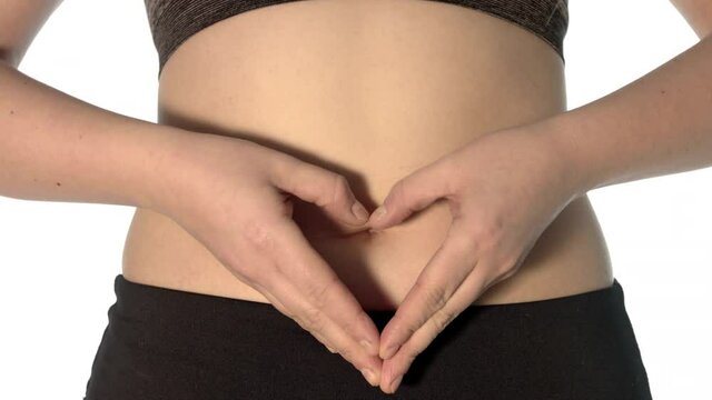 Digestion concept. Woman makes heart shape with hands on her belly. Her stomach is uncovered. Adequate nutrition supports the functioning of the intestines.