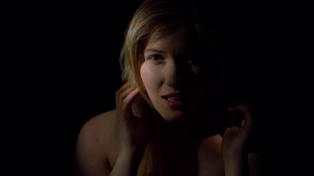 Seductive woman. A young woman, hidden in the shadows, smiles alluringly at the camera. Sexy and tempting. Slowmotion movie.