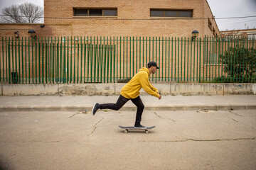 A young male skateboarding on the street in a yellow hoodie and a black cap