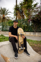 Young caucasian male with a smile sitting on the street holding a skateboard