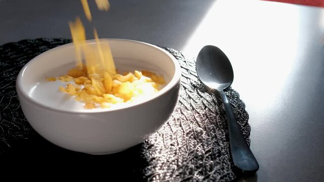 Corn flakes being poured into bowl of milk, slow motion