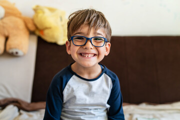 Portrait of happy caucasian boy with eyeglasses sitting at home in room in day real people small male playful child looking to the camera smiling - Powered by Adobe