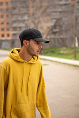 Young caucasian male in a yellow hoodie and black cap standing on the street