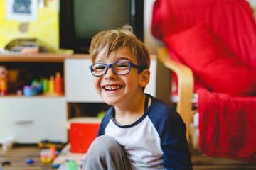 Portrait of happy caucasian boy with eyeglasses sitting at home in room in day real people small...