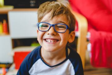 Portrait of happy caucasian boy with eyeglasses sitting at home in room in day real people small male playful child looking to the camera smiling - obrazy, fototapety, plakaty