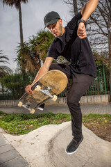 Young caucasian male to in a black shirt and cap jumping with his skateboard