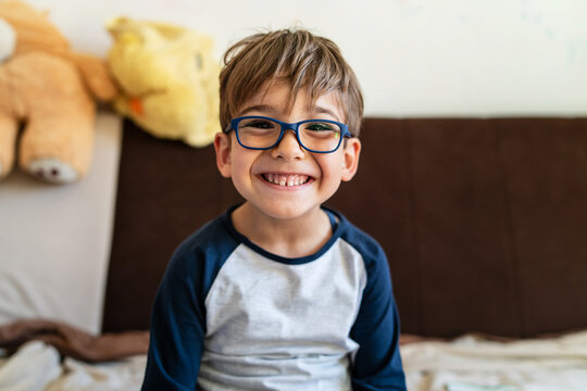 Naklejki Portrait of happy caucasian boy with eyeglasses sitting at home in room in day real people small male playful child looking to the camera smiling
