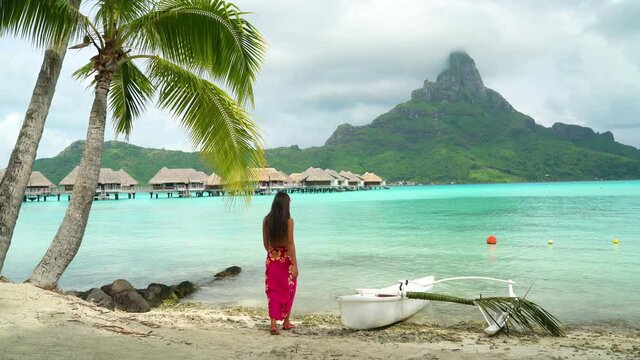 Bora Bora Vacation Travel woman walking on paradise motu beach on in French Polynesia with Mount Otemanu by traditional canoe outrigger vaa. Lady on luxury holiday in overwater bungalow resort hotel