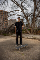 Young caucasian male in a black shirt and cap standing by his skateboard