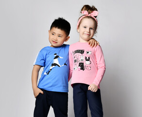 Little cute asian boy and blonde girl hold hands playing hugging on grey background. Happy family close up . brother and sister smiling in pink and blue t-shirts