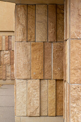 Corner angle view of a modern style rough textured limestone brick wall background with attractive vertical aligned natural kasota stone blocks in varying widths and shades of light brown.