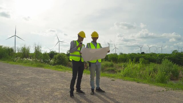 Teamwork of Asian windmill engineer group, worker working, holding a plan on site at wind turbines field or farm, clean energy source. Eco technology for electric power. industry nature. People