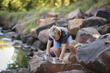 Little boy climbing on and exploring rocks at riverside of Castlereagh River in Coonabarabran, New South Wales, Australia