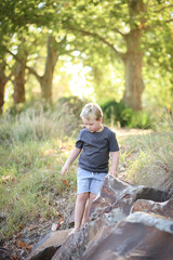 Portrait image of little boy climbing on and exploring rocks at riverside of Castlereagh River in Coonabarabran, New South Wales, Australia