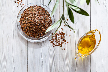 Linseed oil and a bunch of flax seeds on a white wooden table. Modern still life glass ball with oil and linseed, olive branch and copy space.