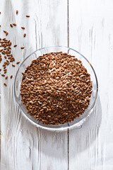 Flax seeds in glass bowl on the white wooden table. Close up and copy space.