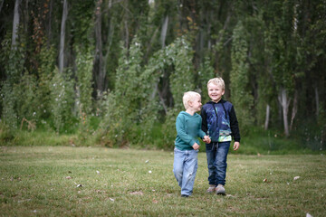 Fototapeta premium Happy little boys walking together in lush green outdoor setting. Brothers having fun in the outdoors.