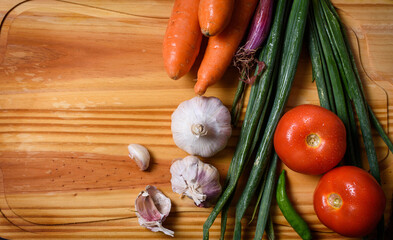 Tabla de madera con cebollas de verdeo, tomates, zanahorias y ajos. Recurso gráfico con motivo vegetariano para escribir en espacio negativo