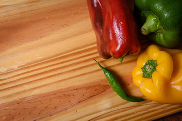 Tabla de madera con pimientos coloridos. Recurso gráfico con motivo vegetariano para escribir en...