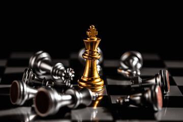 Chess game, the last golden king chess is standing on the chessboard surrounded by several falling silver chess pieces, competition victory, strategy concept.