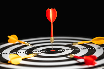 Red dart arrow pining in the target with center of dartboard with yellow dart arrow putting around,...