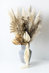 Stylish dried flower arrangement in a cream and blue stripe vase. Including Banksia, Palm Frond, Pampas grass, Native Temp, Ruscus leaves, Stirlingia, and Amaranthus. Photographed on white background.