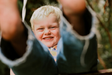 Little blonde boy happily playing on backyard swing. Close up of big smile through feet, action shot
