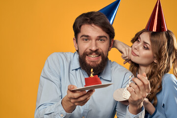 Birthday party man and woman in a cap with a cake on a yellow background cropped view