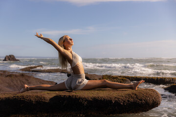 Fototapeta na wymiar Yoga practice. Slim Caucasian woman practicing Hanumanasana, Monkey Pose or Front Split. One arm rasied up. Hamstrings stretching. Beautiful body. Yoga retreat. Beach in Bali, Indonesia