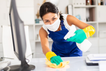 Positive young kazhahstani woman wearing uniform and mask cleaning at company office ..