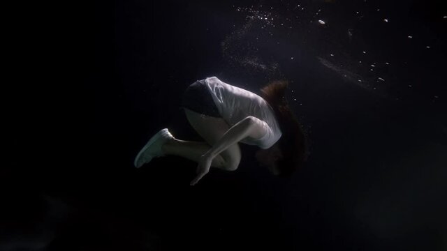 brunette woman is doing somersault inside water of pool or sea, underwater shot