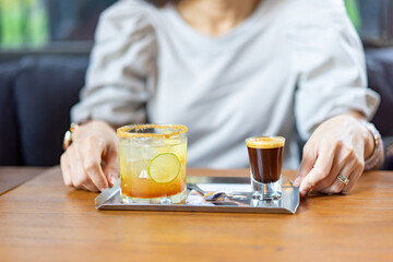A combination between fresh Coffee, Lemon, Orange Soda on the stainless plate on wood table in front of blur woman in Coffee cafe.
