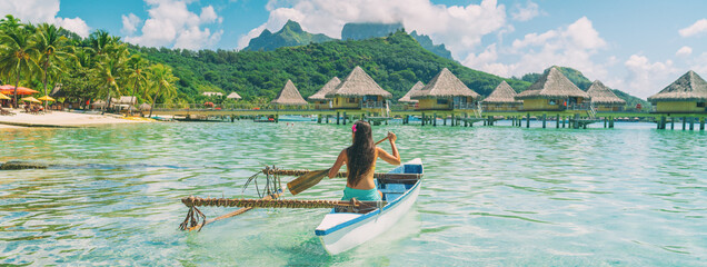 Bora Bora travel vacation iconic photo. Outrigger Canoe - woman paddling in traditional French Polynesian Outrigger Canoe. Mount Otemanu and overwater bungalow resort hotel sport lifestyle - obrazy, fototapety, plakaty