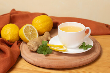 Ginger tea with mint and lemon. Healthy and hot drink. White cup on wooden board on wooden table. Selective focus.