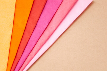a stack of multi colored tissue paper spread out in a fan on a background of brown cardboard.
