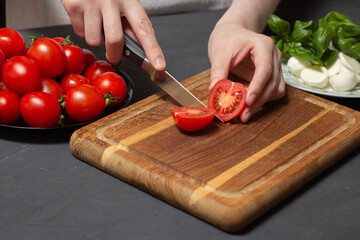 Chef prepare ingredients for homemade cheese pizza. Hands cut cherry tomato with knife on wooden...