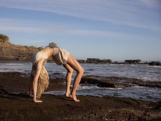 Fototapeta na wymiar Beach yoga. Young slim woman practicing Chakrasana or Urdhva Dhanurasana, Full Wheel Pose. Upward facing bow pose is a deep backbend. Flexible body. Self-care concept. Bali, Indonesia