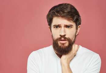 Obraz premium A man with a beard touches his face with his hand on a pink background