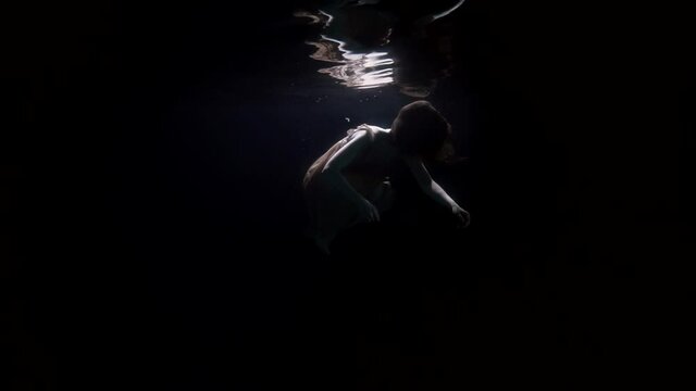 corpse of sunken woman is floating in dark depth, underwater shot of female figure in sea or river