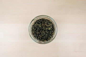 Dried herbal green tea leaves in a glass jar over wooden background